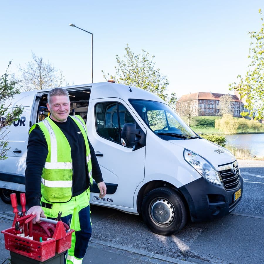 Smiling worker in a hi-vis vest holding tools beside his work van