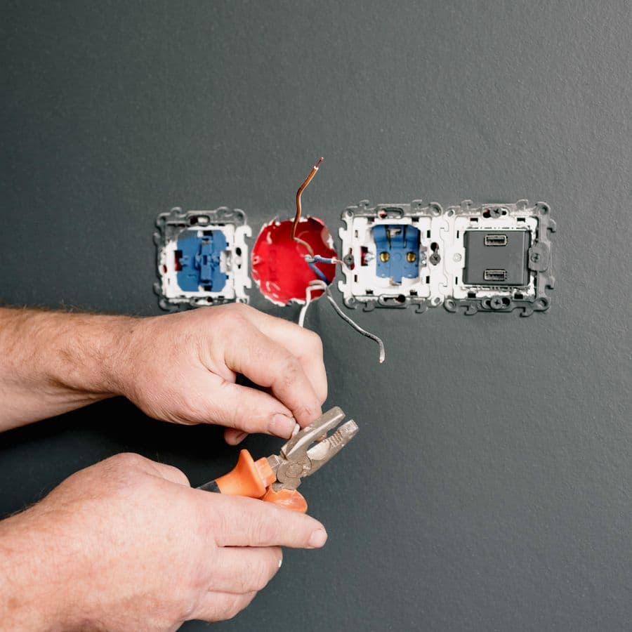 Electrician's hands using pliers to wire an AC socket