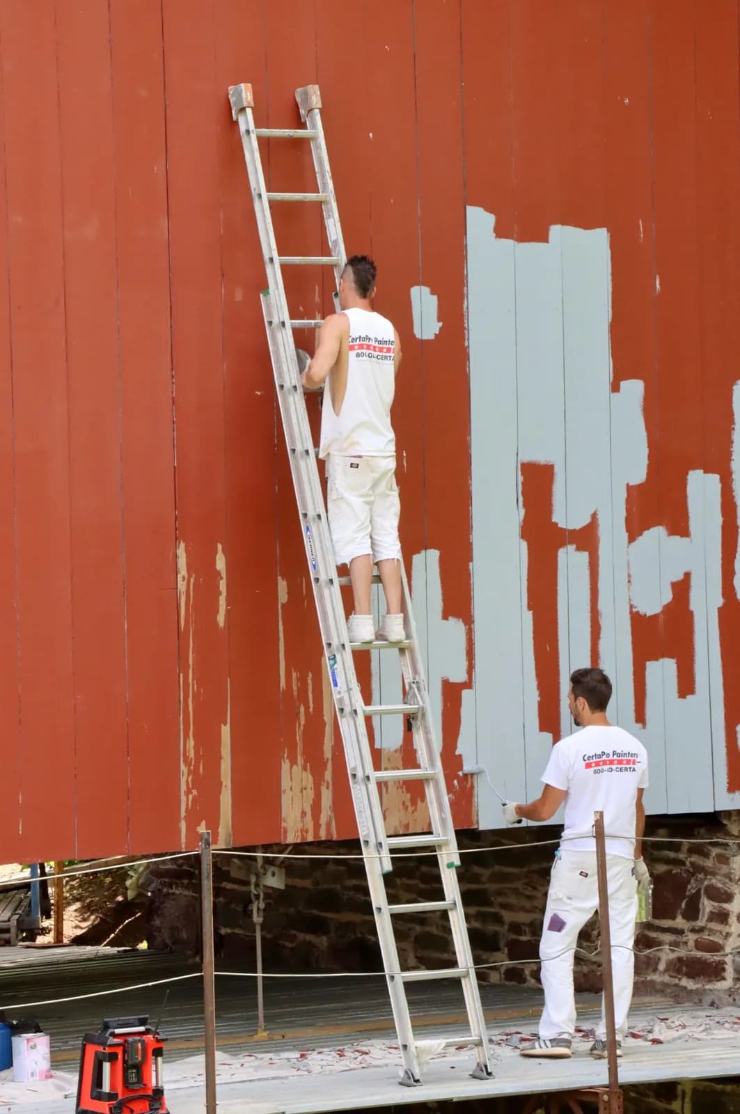 Two decorators in whites repainting an exterior wall from a ladder
