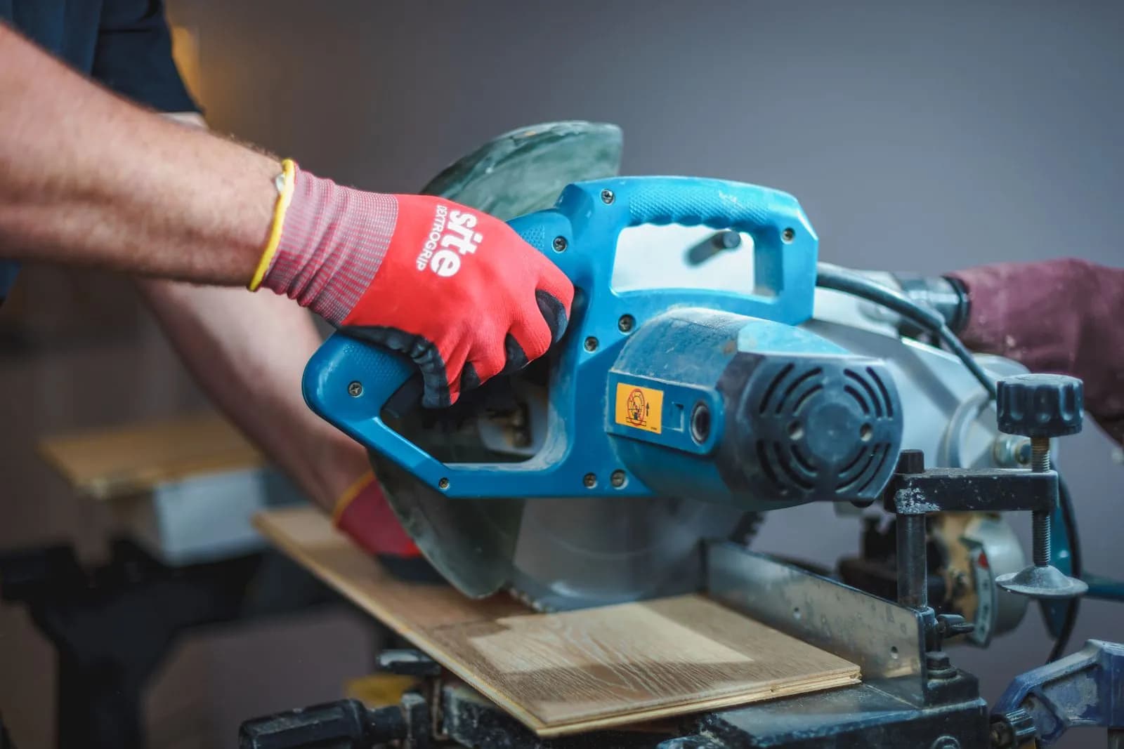 Joiner in work gloves cutting a board on a mitre saw