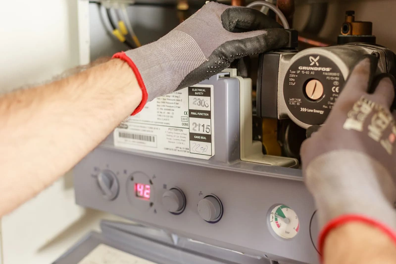 Heating engineer's gloved hands working inside a wall-hung combi boiler
