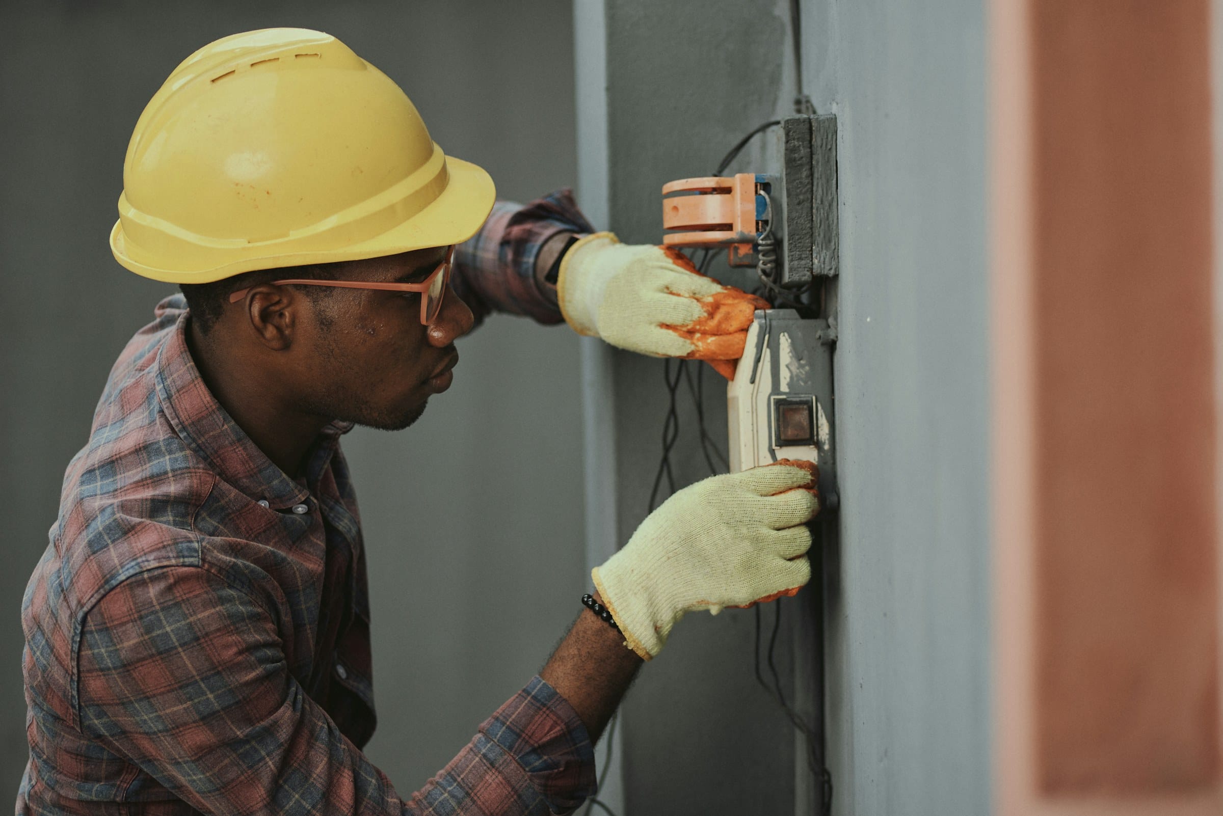 Electrician in a hard hat wiring a wall-mounted unit
