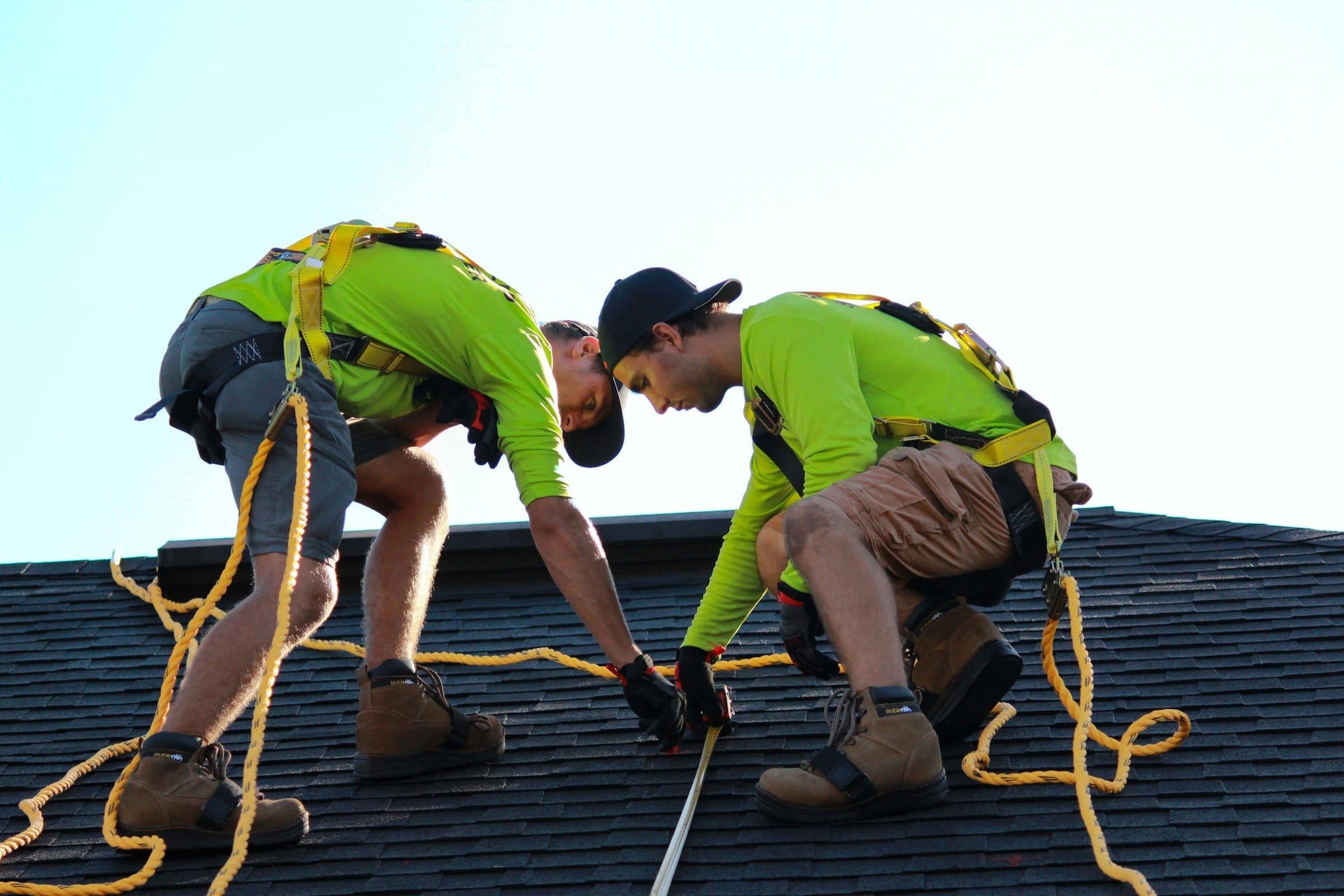 Two roofers in hi-vis and harnesses working on a pitched roof