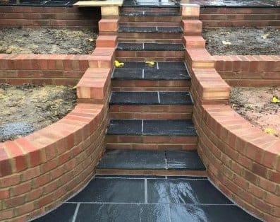 Curved red-brick retaining walls either side of new slate garden steps