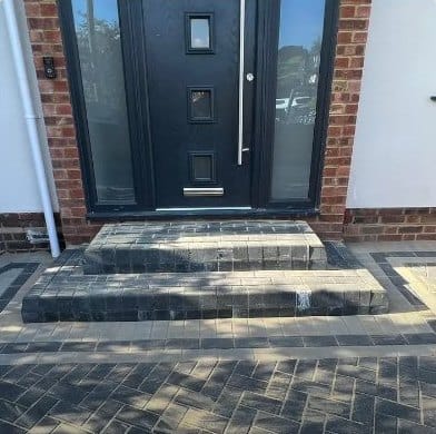Block-paved steps and herringbone driveway outside a black composite front door