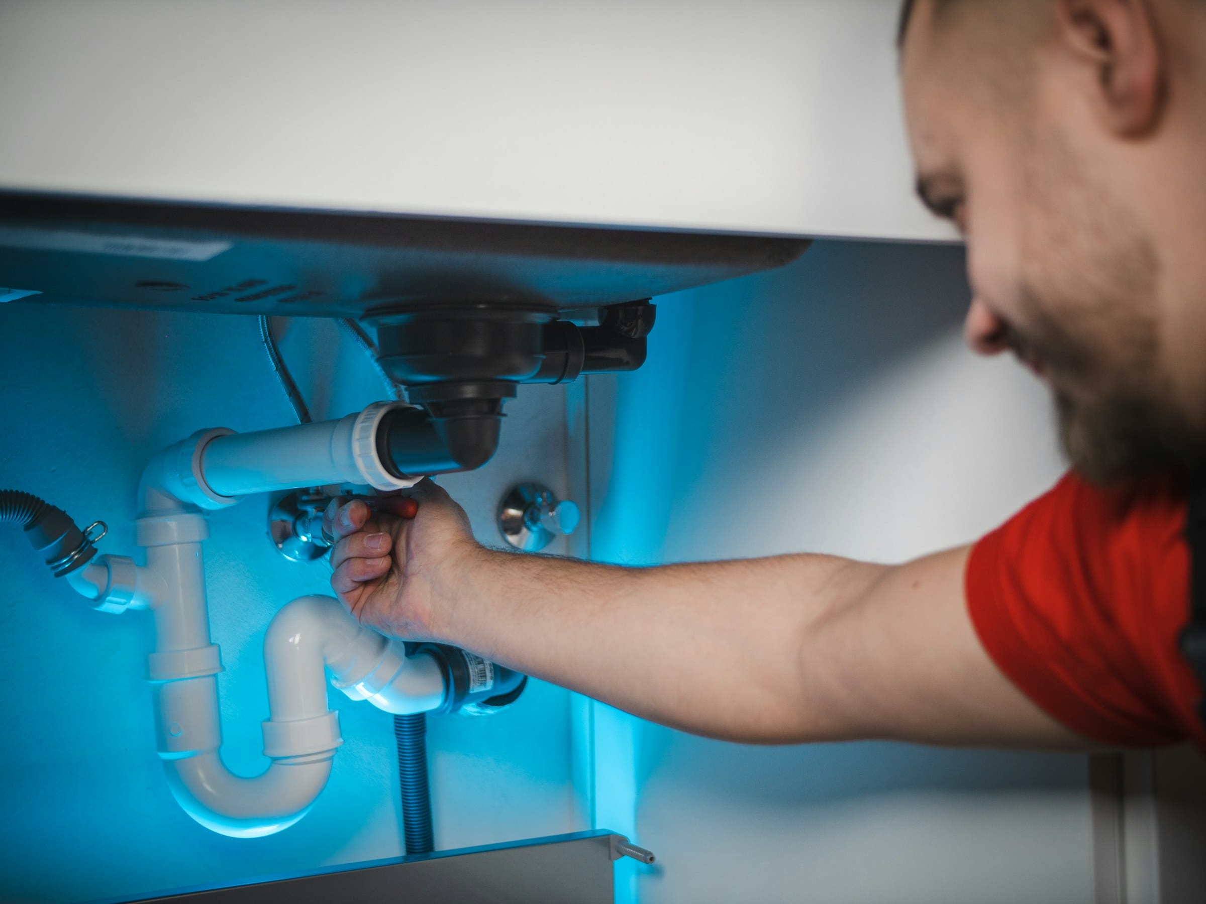Plumber fitting a waste trap under a sink